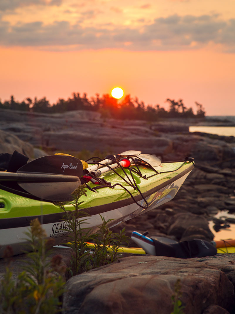 a composite kayak sits on the beach at sunset