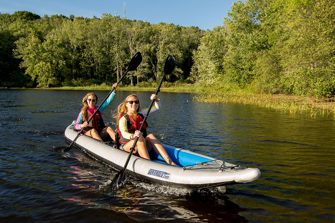 two women paddle an inflatable Sea Eagle kayak on a sunny lake