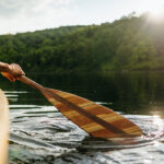person paddles a canoe with a wooden paddle