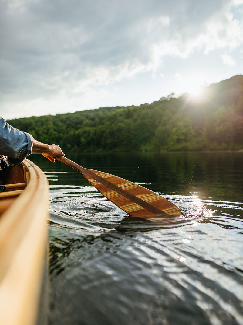 person paddles a canoe with a wooden paddle