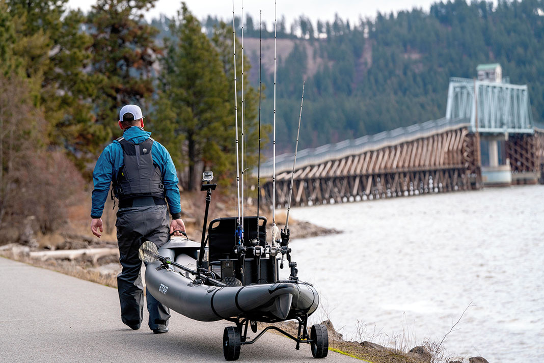 angler pulls his fishing kayak on a cart toward a bridge