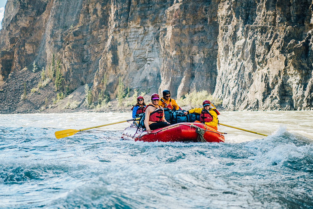 people paddle a red inflatable whitewater raft on the Nahanni River