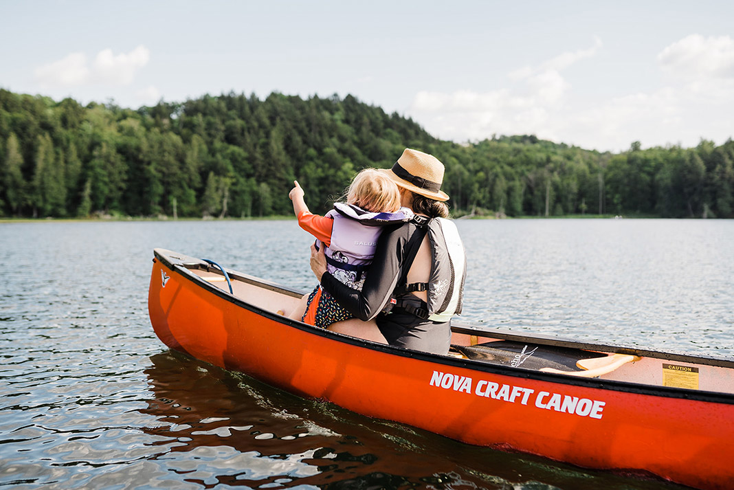 Woman and little girl sitting in bow of red canoe.