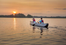 Two people paddling inflatable canoe towards the setting sun on a lake