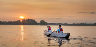 Two people paddling inflatable canoe towards the setting sun on a lake