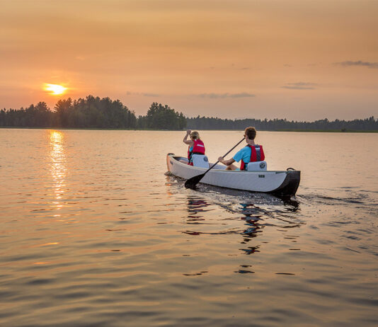 Two people paddling inflatable canoe towards the setting sun on a lake