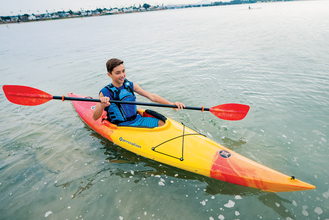 Young boy paddling orange and yellow kayak