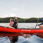 Everything To Know About Nova Craft Canoes Family paddling red canoe across a lake.