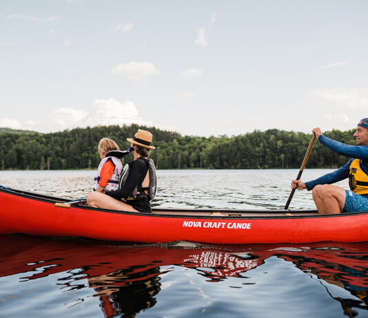 Family paddling red canoe across a lake.