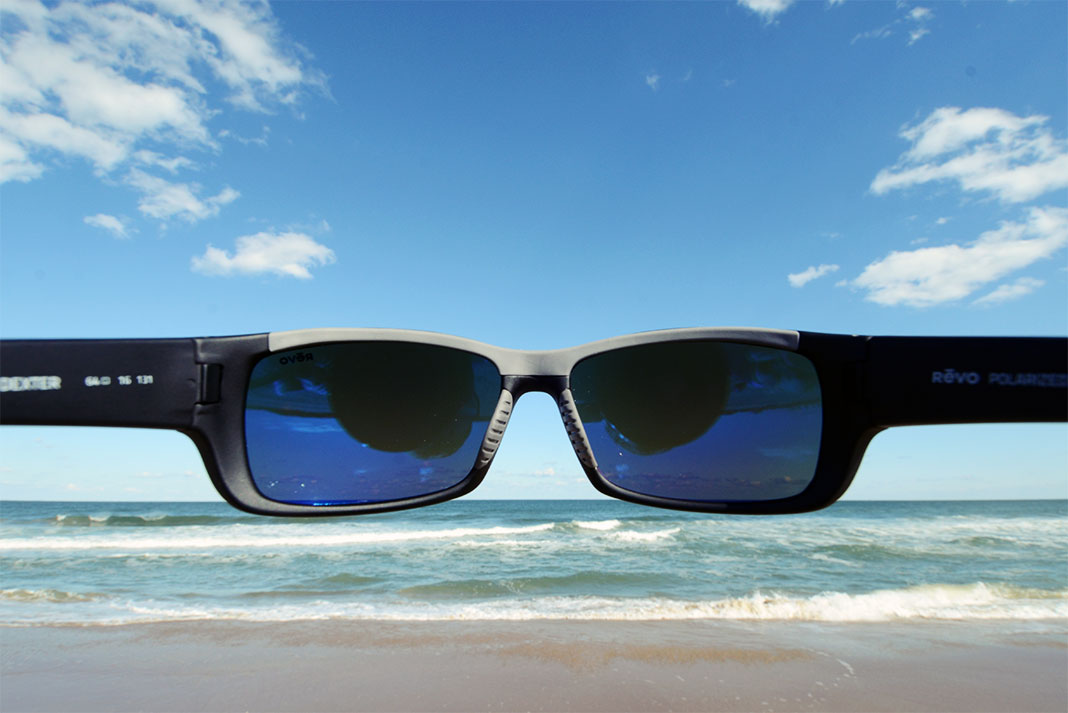 looking out at a sandy beach with surf rolling in through a pair of sunglasses