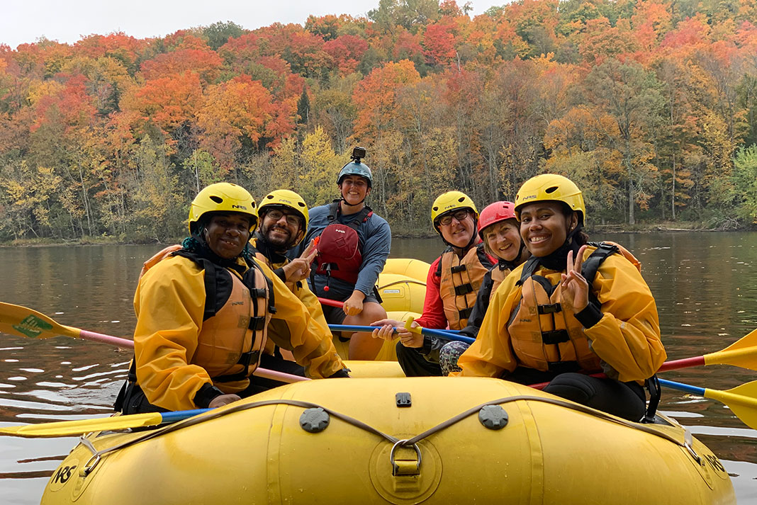 a group of river rafters pose in a yellow raft in front of fall foliage