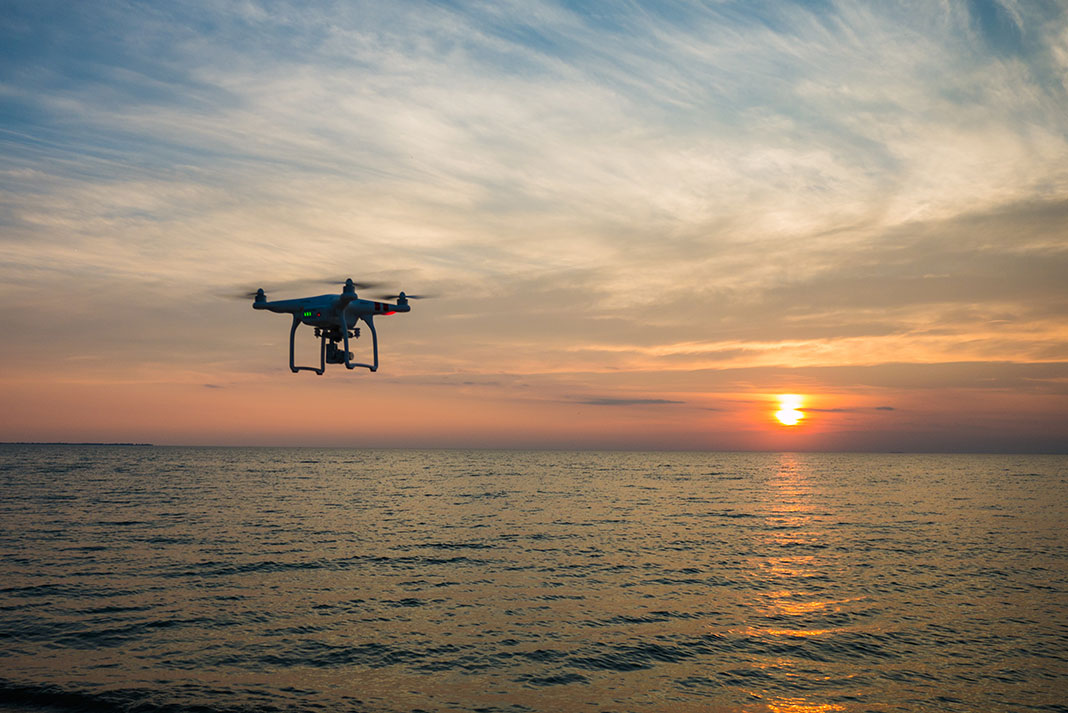 drone flies over water at sunset