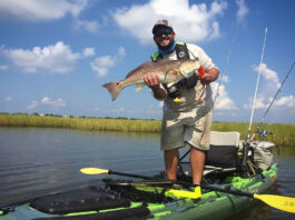 man stands on kayak and holds up redfish caught in Louisiana