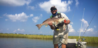 man stands on kayak and holds up redfish caught in Louisiana