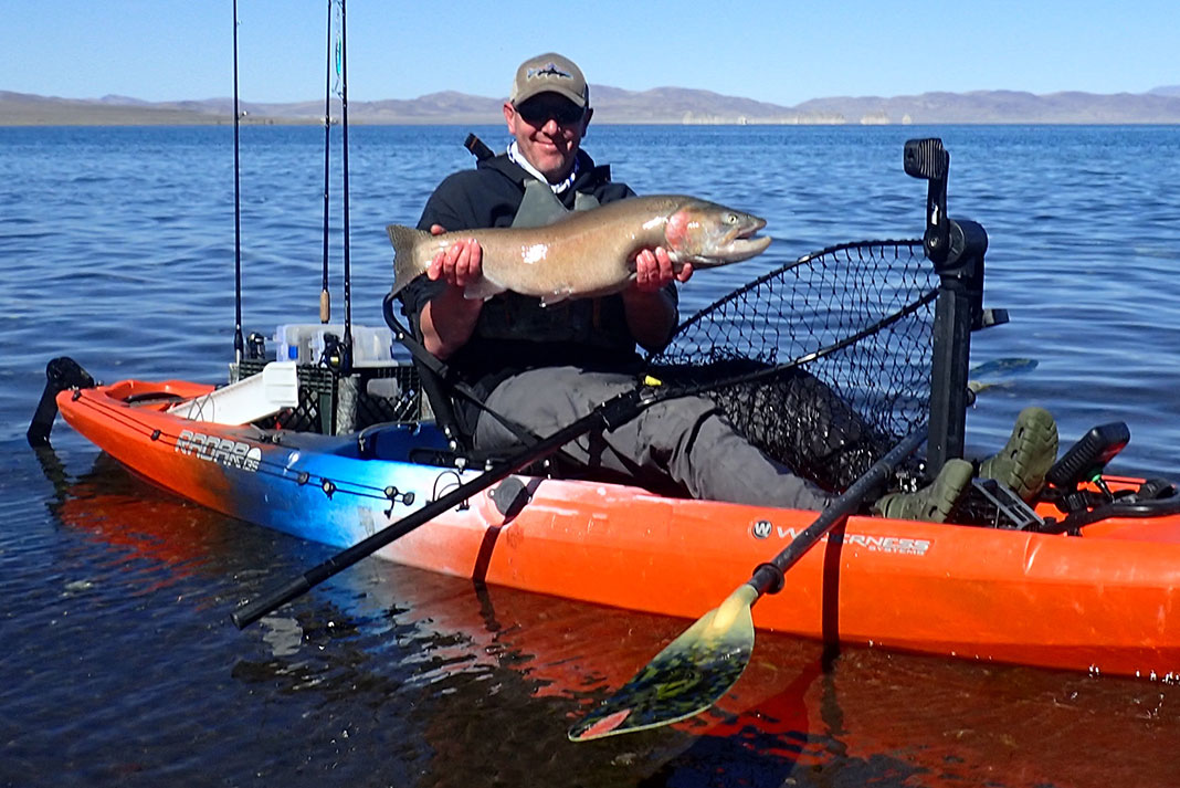 man in red fishing kayak holds up fish caught in Nevada