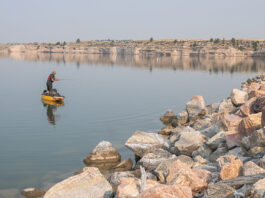 man standup fishing from a kayak in front of a rocky shore in Wyoming