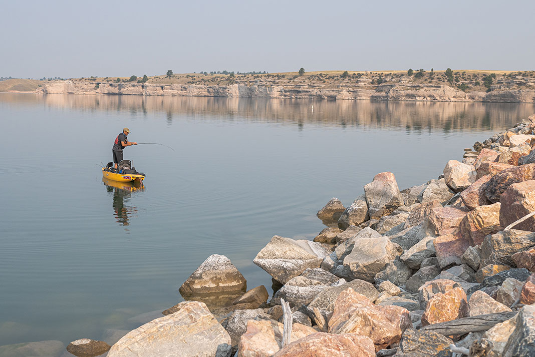 man standup fishing from a kayak in front of a rocky shore in Wyoming