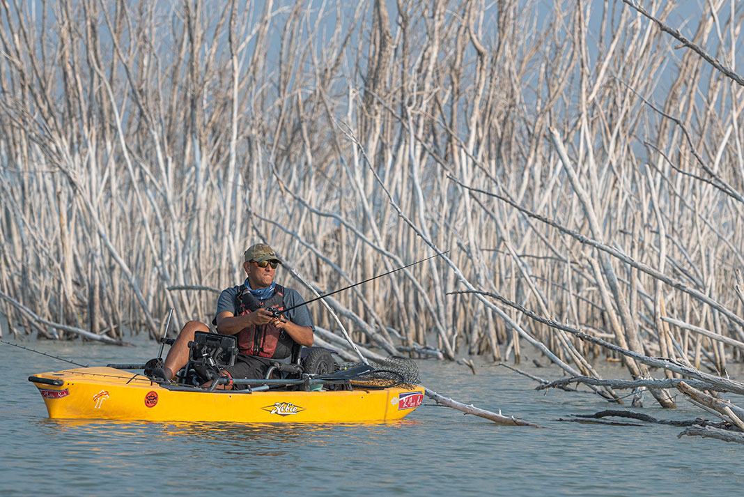 man fishes from yellow kayak in front of white branches