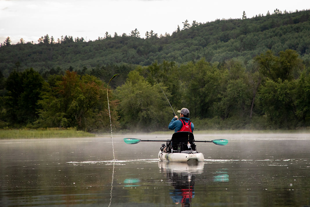 man sits and casts his fishing rod from a paddle kayak