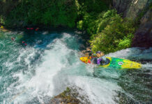 a female whitewater kayaker runs a waterfall while her paddling crew watches from below
