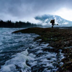 10 Pros On The Hardest River Moves You’ll Ever Make a whitewater kayaker hauls his boat away from a dusky, cloudy river after practising river moves