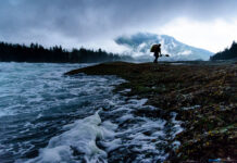 a whitewater kayaker hauls his boat away from a dusky, cloudy river after practising river moves