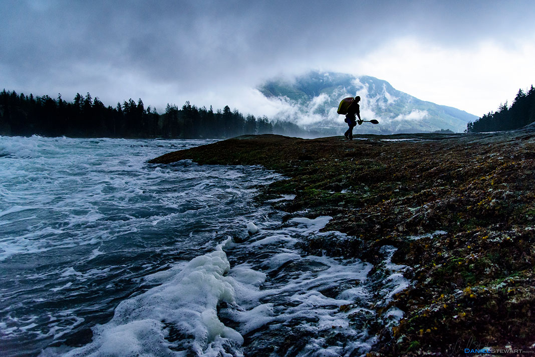 a whitewater kayaker hauls his boat away from a dusky, cloudy river after practising river moves