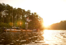 a man fishes within his budget while standing and casting from his fishing kayak at dawn