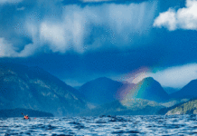 a long distance expedition kayaker paddles the cloudy Kyuquot Crossing in front of a rainbow