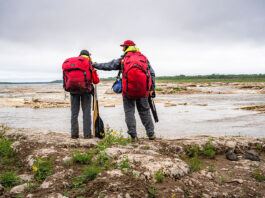 a man and woman stand beside a northern river wearing Ostrom Outdoors canoe packs