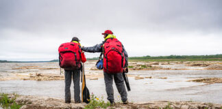 a man and woman stand beside a northern river wearing Ostrom Outdoors canoe packs