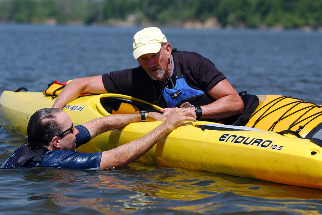 man instructs a recreational kayaker on how to re-enter his kayak