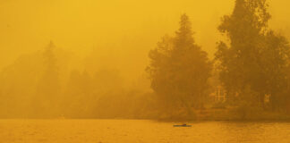 a paddler kayaks in the hazy yellow wildfire light of the summer season