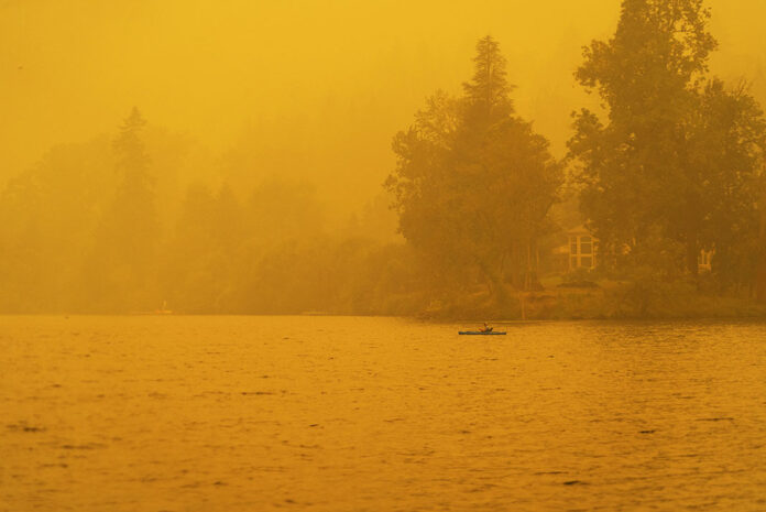 a paddler kayaks in the hazy yellow wildfire light of the summer season