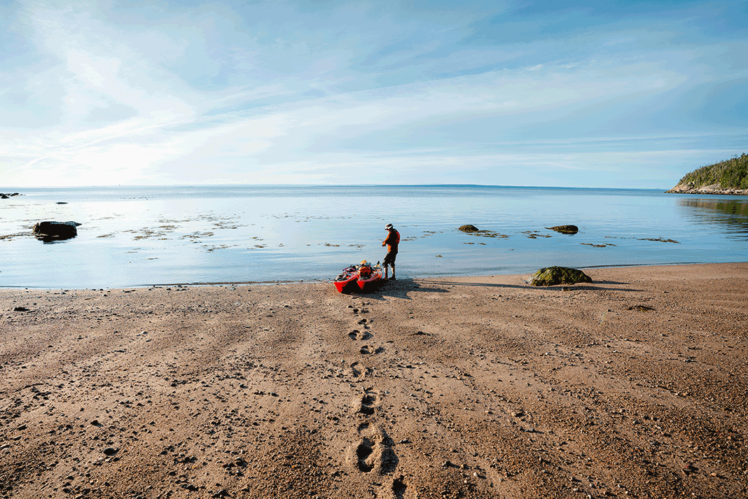 man drags a kayak across a sandy beach to the water