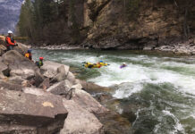 a whitewater rescuer leaps into the river to save a kayaker using rescue gear