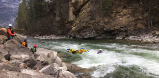 a whitewater rescuer leaps into the river to save a kayaker using rescue gear
