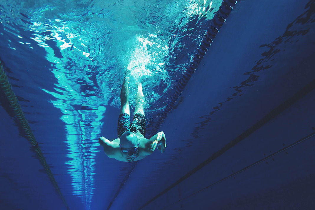 a male athlete dives underwater in a pool