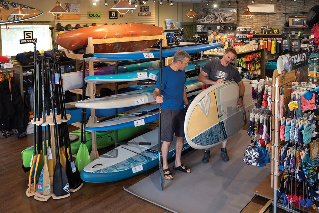 two people look at paddleboards in a paddle shop