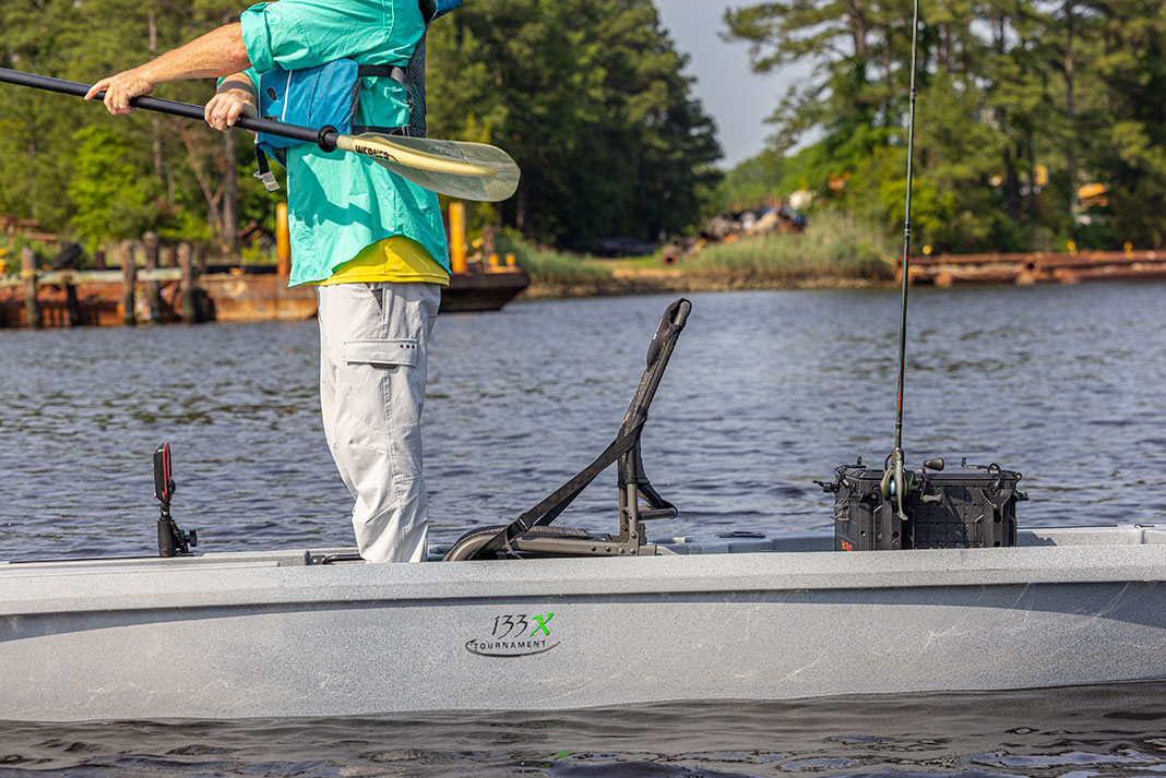 man stands and holds a paddle in an Ascend 133X fishing kayak