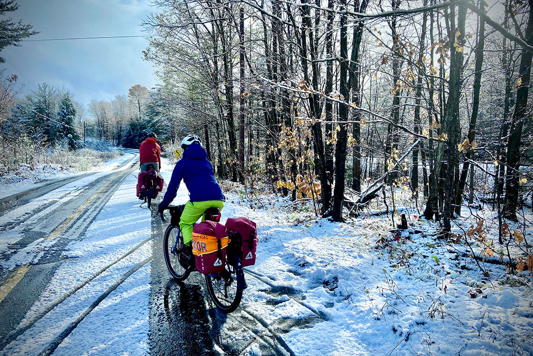 two people cycle long-distance along a somewhat snowy forest road in early winter