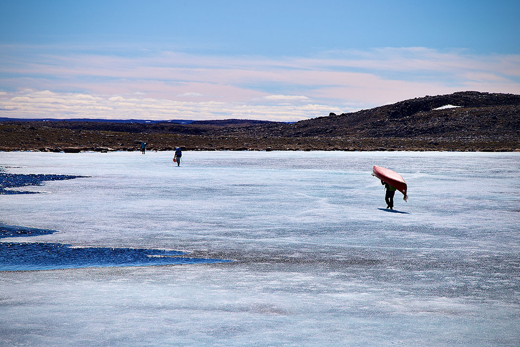 people portage canoes across Arctic ice with stony hills in the background
