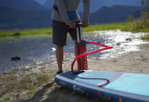 a person pumps up an inflatable paddleboard in front of water and hills
