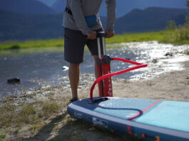 a person pumps up an inflatable paddleboard in front of water and hills