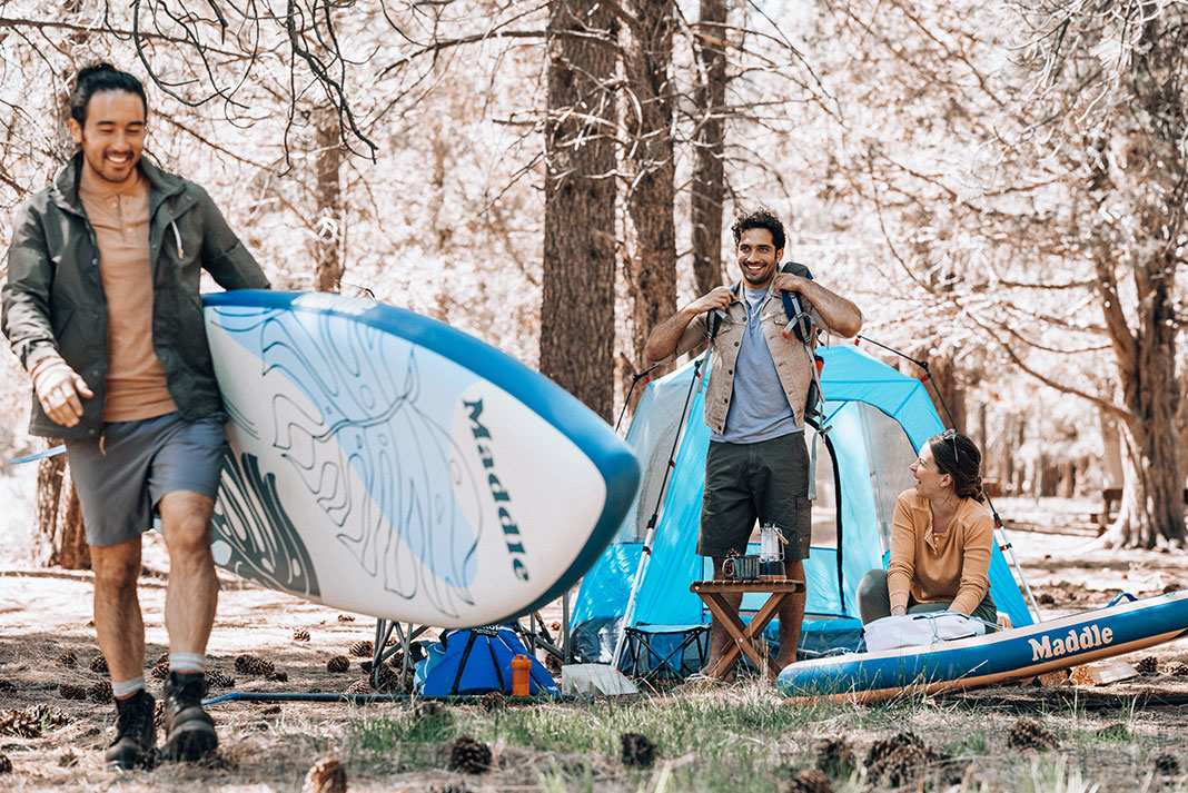 three people at a campsite prepare their inflatable paddleboards