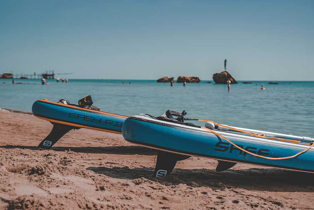 two inflatable paddleboards sit on a sandy beach