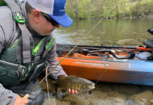 man lifts a smallmouth bass caught using crankbait tactics out of the river