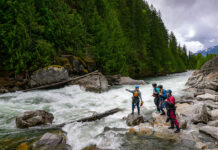 a group of female whitewater paddlers scout a river while wearing womens drysuits