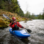 Whitewater Kayak Review: Zet Chili man paddles the Zet Chili whitewater kayak beside a mossy riverbank