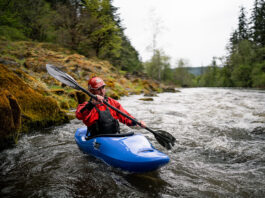 man paddles the Zet Chili whitewater kayak beside a mossy riverbank